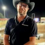 A man in a cowboy hat standing in a rodeo arena