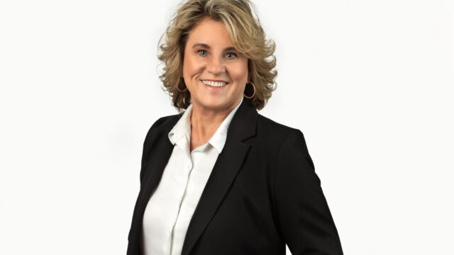 Professional woman in a black blazer and white shirt smiling against a white background.