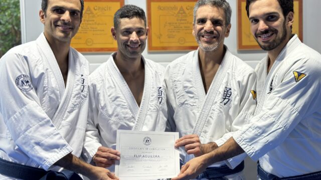 Four men in white judo uniforms smiling and holding a certificate.