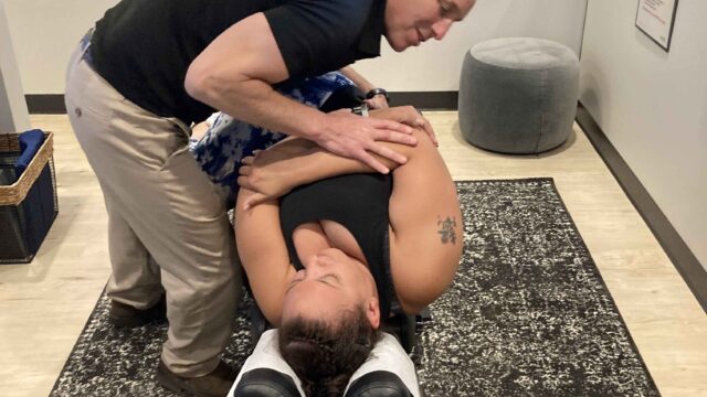 A chiropractor performs an adjustment on a person lying on their side on a treatment table in an office setting.