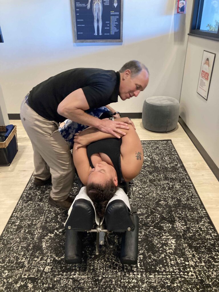 A chiropractor performs an adjustment on a person lying on their side on a treatment table in an office setting.