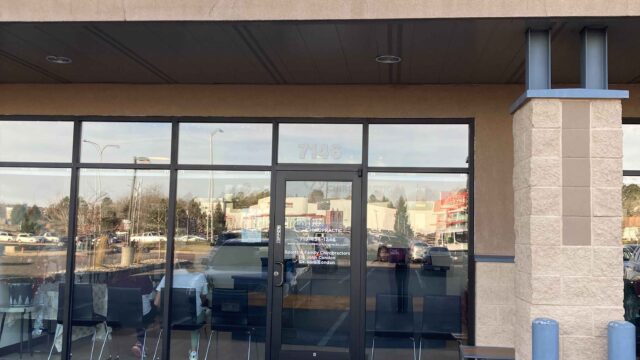 Storefront of "The Wellness Way" with a glass entrance, located in a parking lot. A sign with a puzzle piece logo is displayed above.