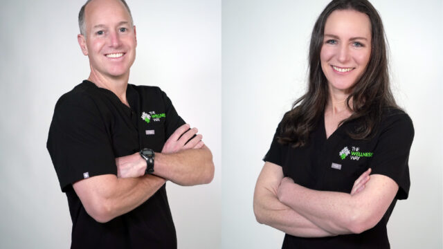 Dr John and Dr Lara Condon of The Wellness Way in black uniforms with "The Wellness Way" logo, standing with arms crossed against a plain background.