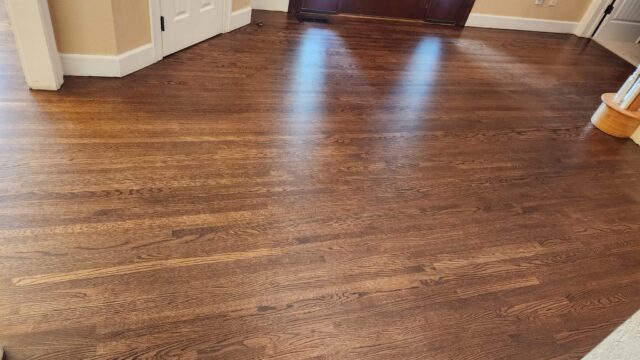 A room with polished, dark-stained hardwood flooring, white door trim, beige walls, and natural light reflecting off the floor.